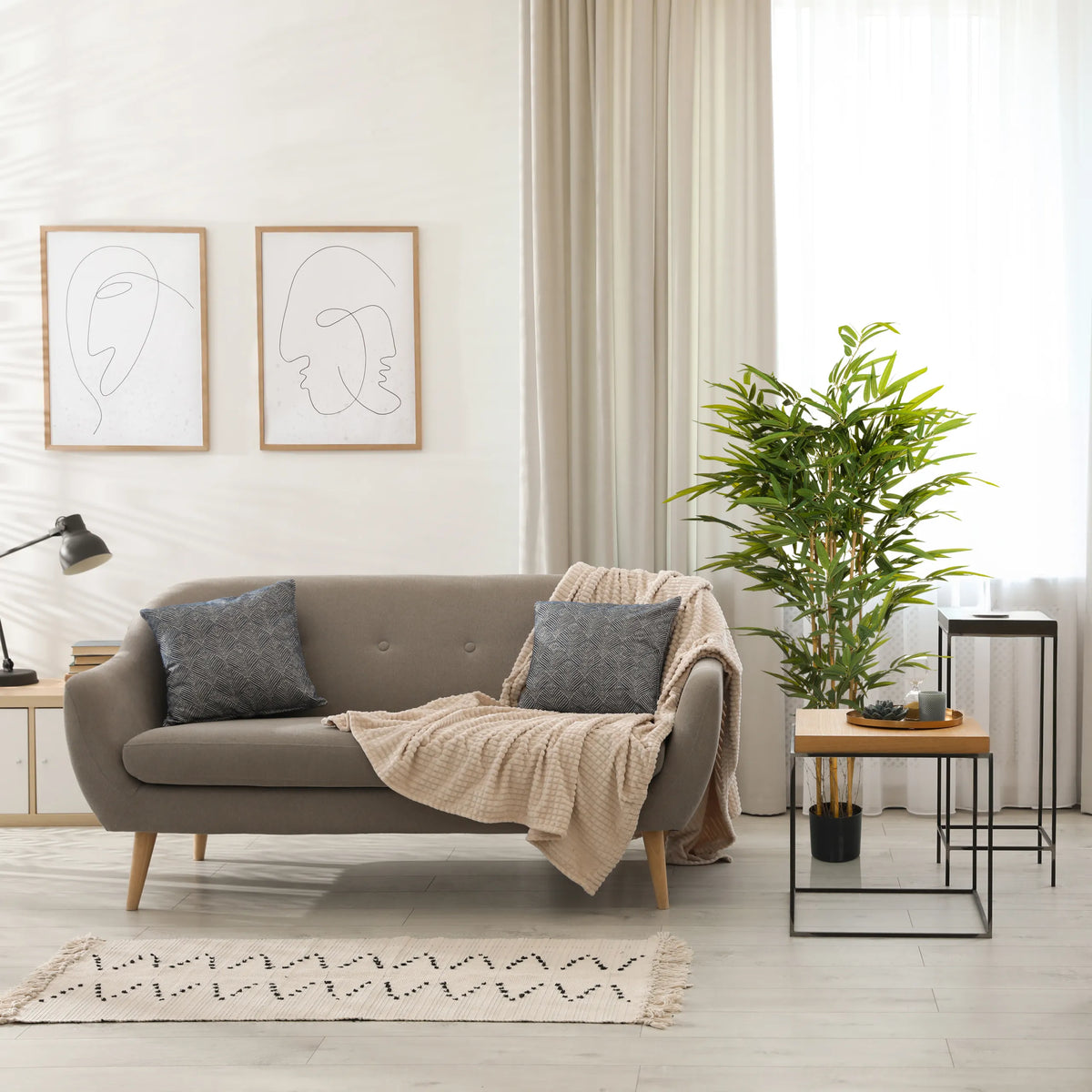 Grüne Kunstpflanze BAMBUS II in einem schwarzen Topf neben einem Sofa von hjh OFFICE