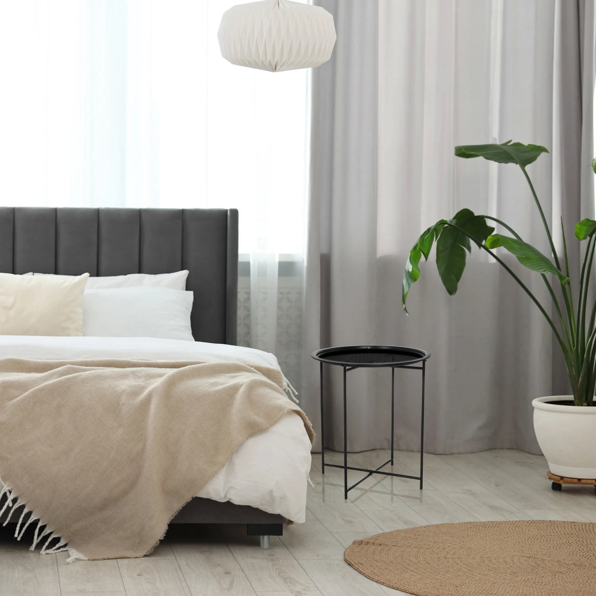Table d'appoint ALLRUND noire en métal avec un plateau perforé à côté d'un lit de hjh LIVING