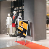 Support d'affiche AGENDA II en aluminium comme stop-trottoir avec une affiche publicitaire jaune dans un espace de vente de hjh OFFICE