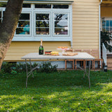 Table pliante blanche EASY UP MULTI II de 152 x 70 cm sur une pelouse devant une maison de hjh OFFICE