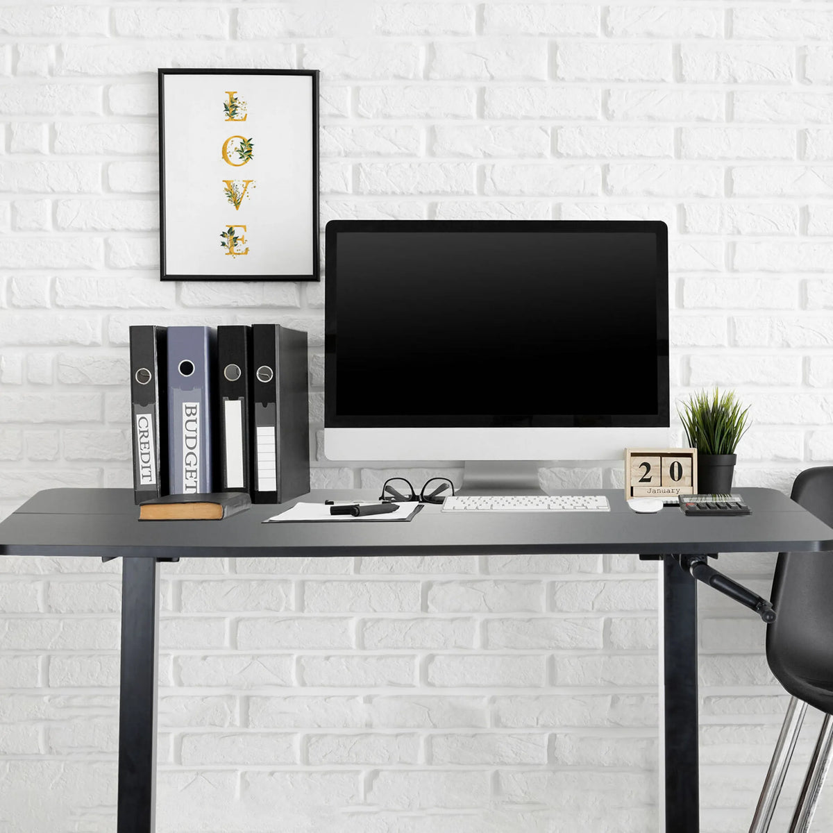 Bureau assis-debout noir STAND CR avec écran, clavier et classeurs devant un mur de briques blanches de hjh OFFICE