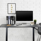 Bureau assis-debout noir STAND CR avec écran, clavier et classeurs devant un mur de briques blanches de hjh OFFICE