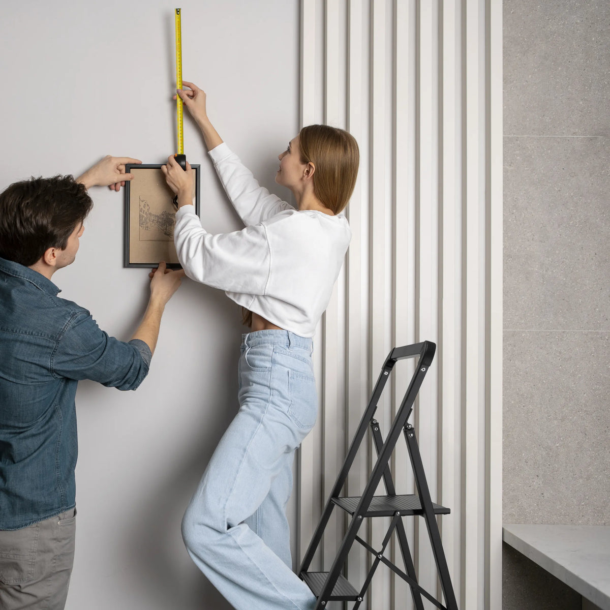 Échelle pliante SOLID W6 noire à trois marches utilisée pour accrocher un tableau de hjh OFFICE