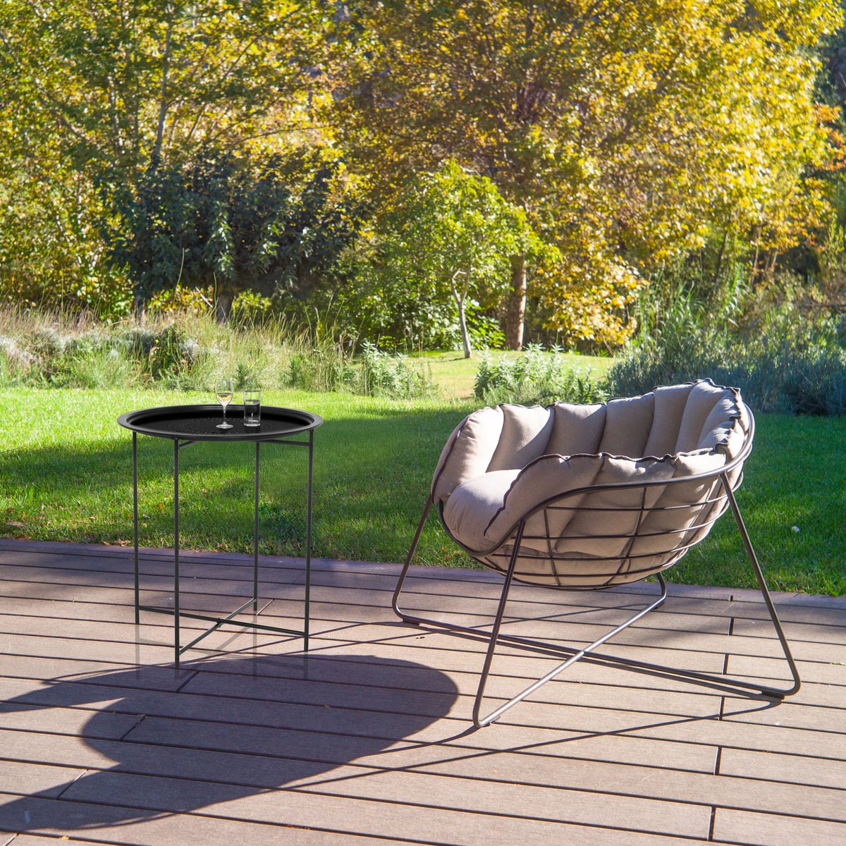 Table d'appoint ALLRUND en métal noir avec motif perforé sur une terrasse à côté d'un fauteuil de détente de hjh LIVING