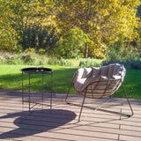 Table d'appoint ALLRUND en métal noir avec motif perforé sur une terrasse à côté d'un fauteuil de détente de hjh LIVING